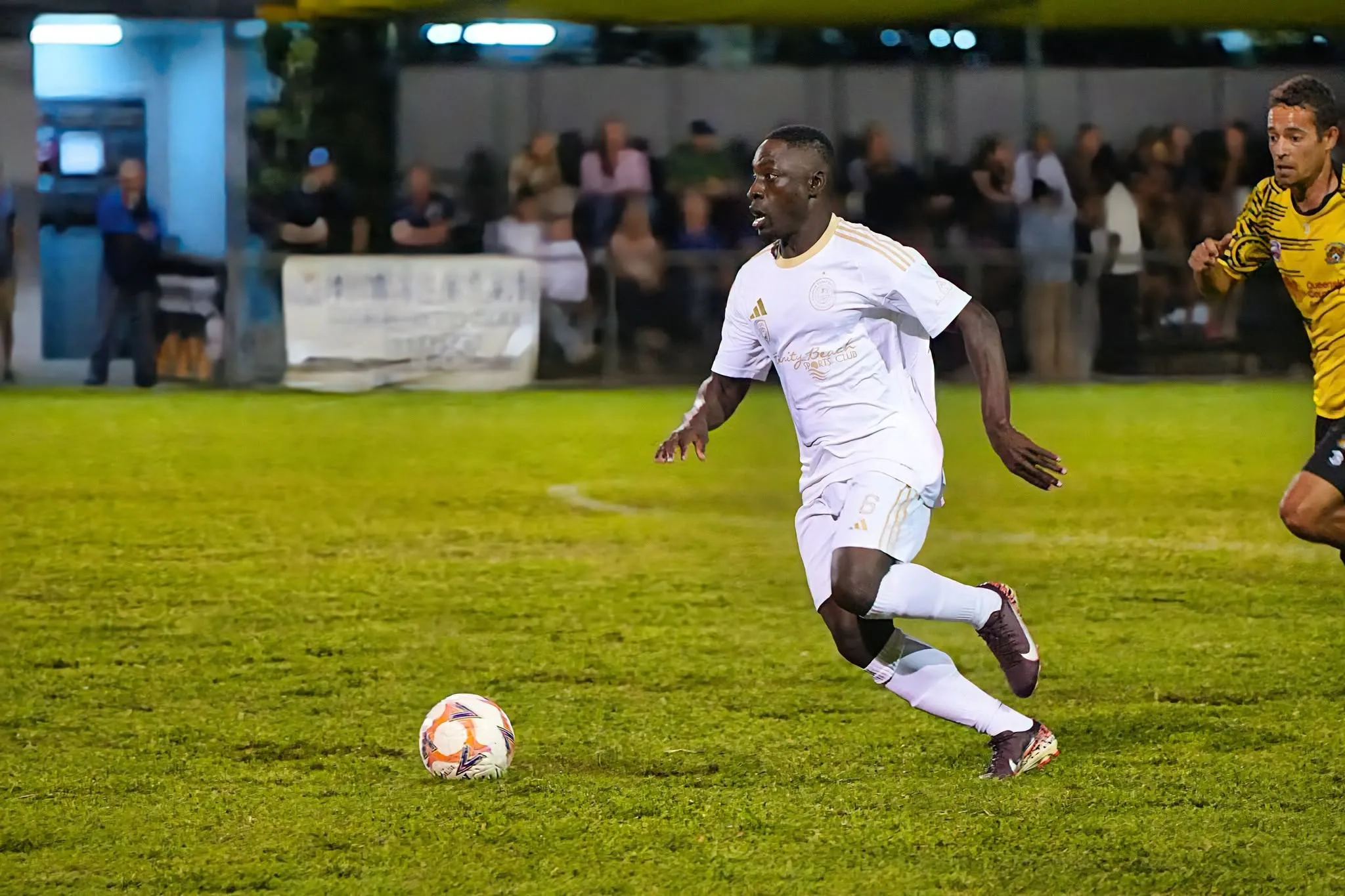 A Marlin Coast Rangers senior player driving forward with the ball under lights in front of a full sideline