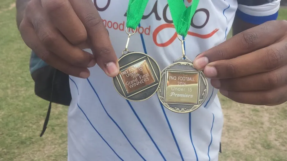A player holding two FNQ Football Under 15 medals, a Grand Final winners medal and a Premiers medal
