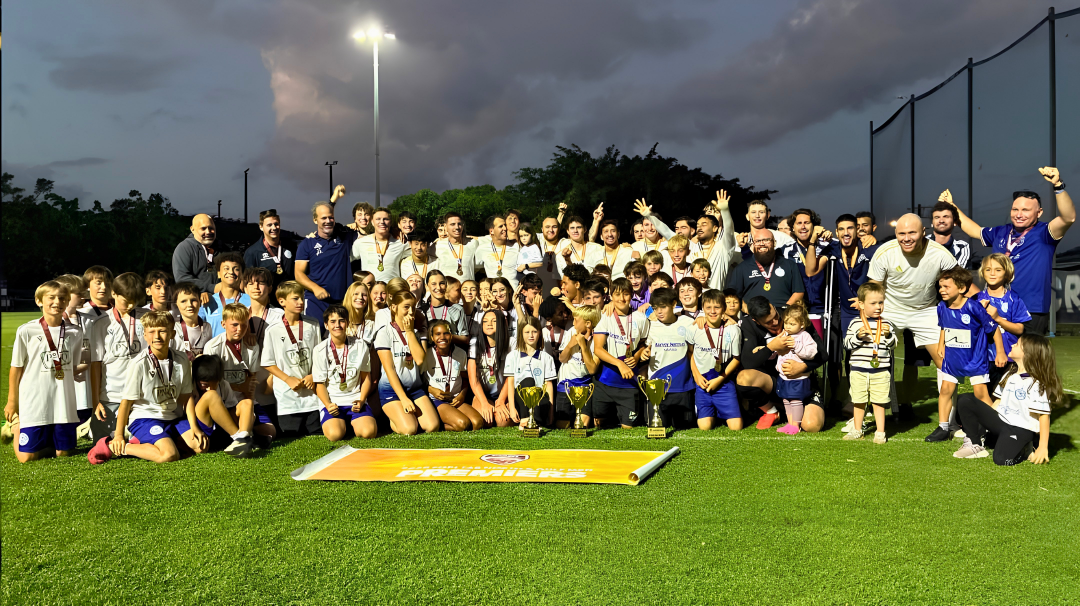 Marlin Coast Rangers players, coaches and families from across the club celebrating with premiers trophies under lights at Pennell Field, Cairns